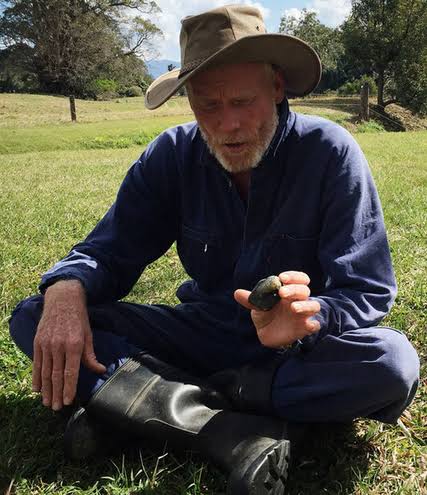 James McKenzie crouching on grass in work clothes and hat, holding a small freshwater turtle